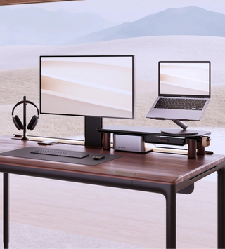 Modern beflo Tenon office setup with a computer monitor, laptop, keyboard, mouse, and headphones on a wooden desk.